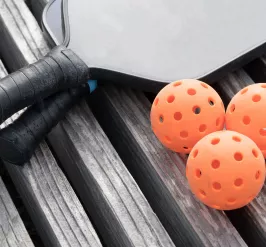 Two pickleball paddles and three balls sitting on a wooden surface.