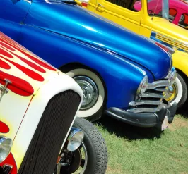 Colorful vintage cars are lined up in the grass.