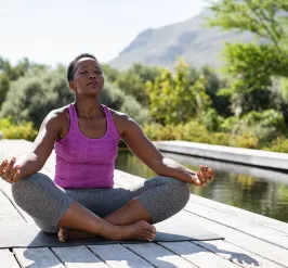 A woman sitting outdoors in a relaxed yoga pose. Her eyes are closed.