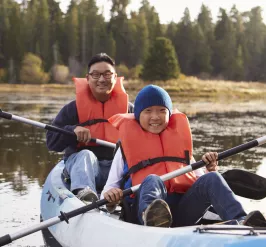 A father and son wearing life vests while kayaking.
