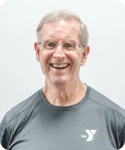 A portrait of John Odland, a personal trainer at the Ragsdale YMCA. He is wearing glasses and a gray shirt and smiling at the camera.
