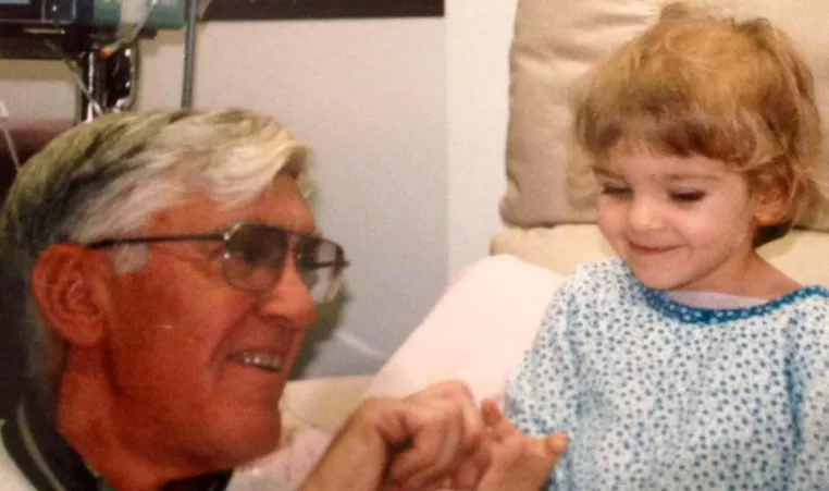 A little girl in the hospital smiles with her grandfather.