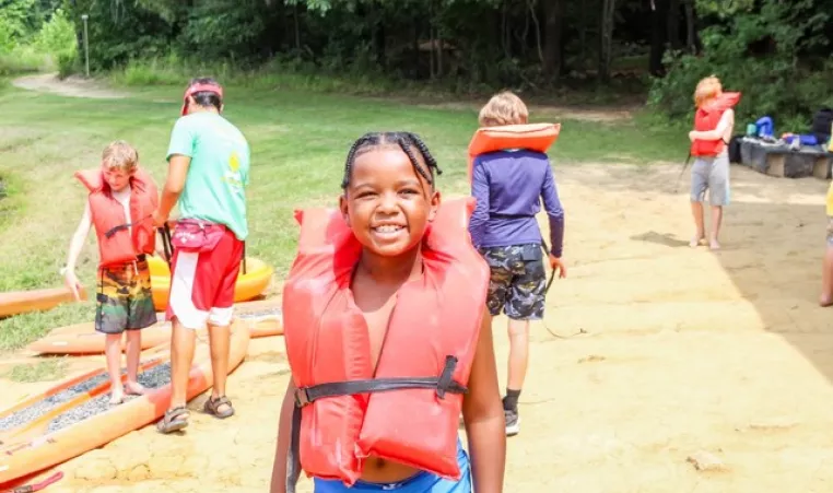 Kid with an orange lifejacket at summer camp.