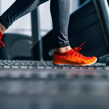 A person wearing gray exercise pants and orange and red shoes walks on a treadmill.