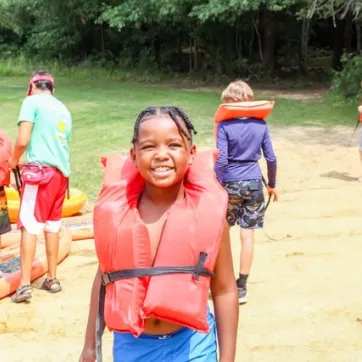 Kid with an orange lifejacket at summer camp.