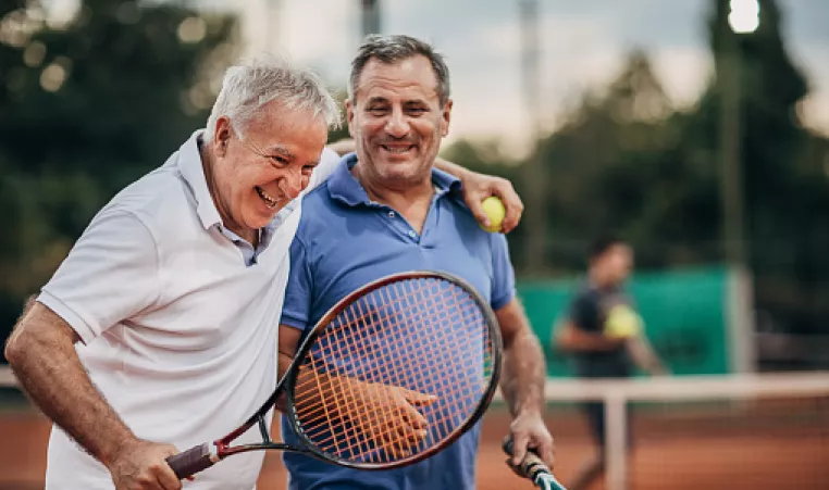 Two older adults laughing and bonding during tennis match.