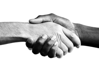A black and white photo of a handshake from people of two different ethnicities. One of the hands is dark-skinned and the other hand is light-skinned.