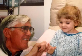 A little girl in the hospital smiles with her grandfather.