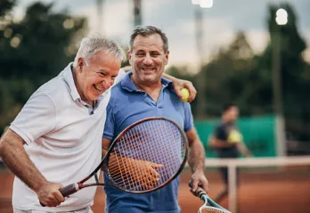 Two older adults laughing and bonding during tennis match.