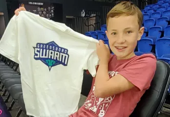 Young boy at a basketball game along the sidelines holding up team tshirt