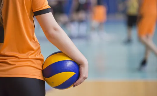 A girl holds a blue and yellow volleyball at her side.