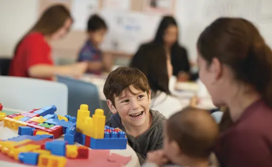 A young boy playing with building blocks smiles.