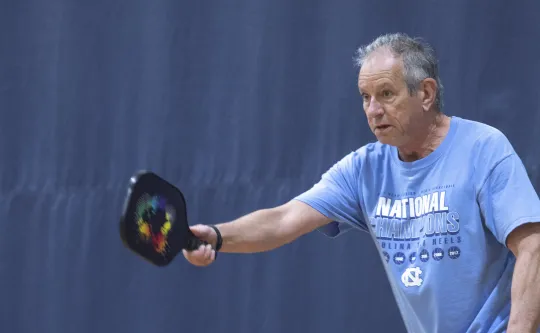 A man playing pickleball at the Ragsdale Y. He is wearing a blue shirt and preparing to send the ball back to his opponent.