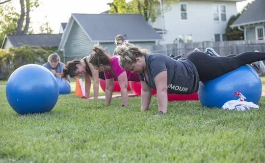 A group of women in an outdoor group exercise class at the Reidsville YMCA. They are balancing on exercise balls.