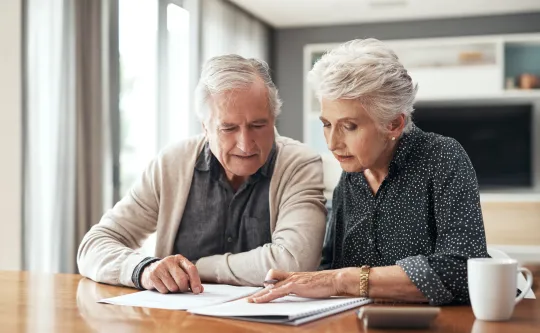 A senior man and senior woman looking at information on paper and a notebook.