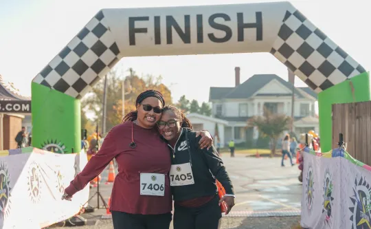 Two women standing together at the finish line during the Reidsville Family YMCA's Turkey Trot road race. They are smiling at the camera.