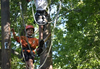 A boy smiles as he climbs on a ropes course.