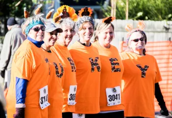 A group of women standing together. They are each wearing orange shirts with a letter on them. The shirts spell out "tirkey."