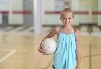 A little girl smiling at the camera while holding a volleyball.