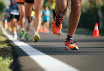 A cropped photo of people running a race on a road. Only their legs and shoes are visible.