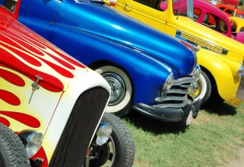 Colorful vintage cars are lined up in the grass.