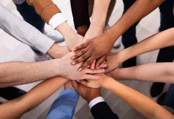 A diverse group of people standing with their hands in a circle.