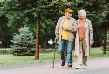 A pair of seniors walking together and smiling. A senior man is walking with a cane.