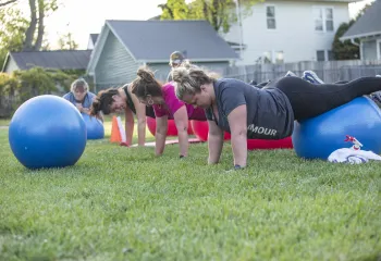 A group of women in an outdoor group exercise class at the Reidsville YMCA. They are balancing on exercise balls.
