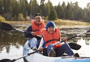 A father and son wearing life vests while kayaking.