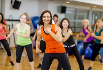 A woman exercising in a group exercise class smiles at the camera.