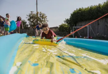 A group of children having fun outside on a slip and slide.
