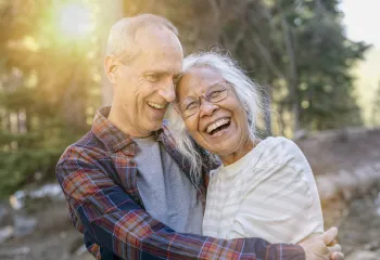 A senior man and woman outdoors laughing together.