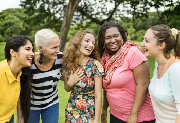 A group of diverse women standing outside together and laughing.