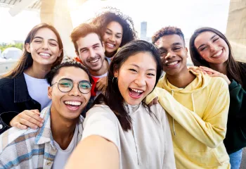 A diverse group of teens laughing together. They are smiling into the camera and taking a selfie.