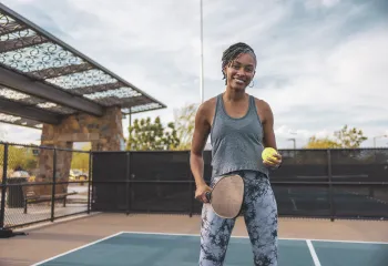 A woman holding a pickleball paddle stands outside on a court.