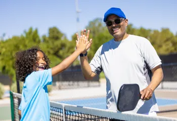 A father and young child playing pickleball together.