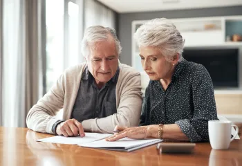 A senior man and senior woman looking at information on paper and a notebook.