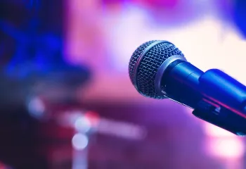 A close-up image of a microphone. There is a purple and blue background behind it.