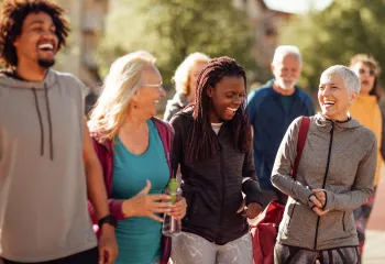 A diverse group of people outdoors wearing exercise clothing. They are laughing together.