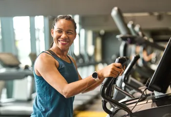 A woman at the gym exercising on a machine. She is smiling.