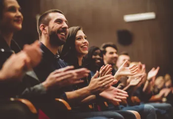 A close up photo of a row of audience members in an auditorium. They are clapping.