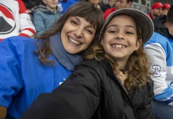 A mother and daughter taking a selfie together at a hockey game. They are smiling into the camera.