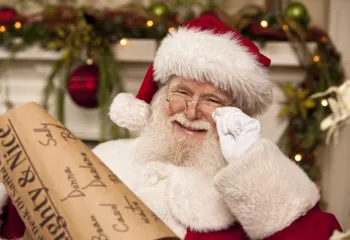 A man dressed as Santa Claus smiling at the camera. He is holding a list.