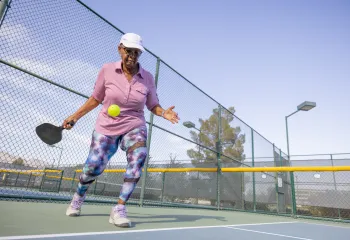 A senior woman playing pickleball outdoors.