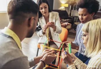 A group of adults sitting together and building a structure out of colorful sticks.