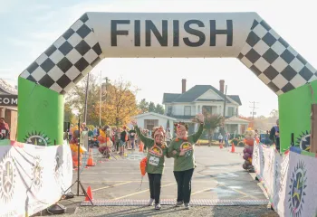 Two Turkey Trot runners arms interlocked, celebrating together as they cross the finish line.