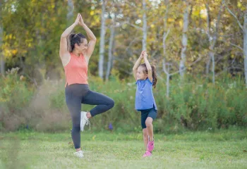 A mother and young daughter doing yoga together outside.