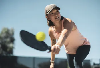 A woman wearing a hat plays pickleball outdoors.