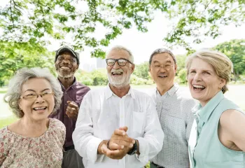A diverse group of seniors standing together outdoors. They are smiling at the camera.