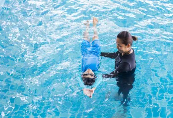 A swim lesson instructor teaching a young child how to swim in the pool.